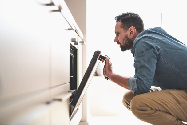 Young bearded man checking oven in kitchen - Φωτογραφία, εικόνα