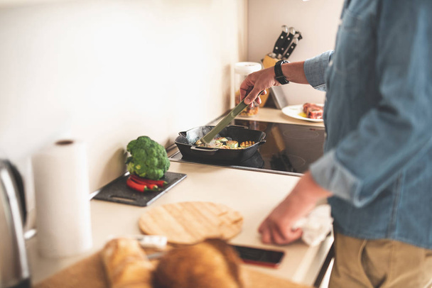 Man using tongs while cooking zucchini in kitchen - Foto, afbeelding
