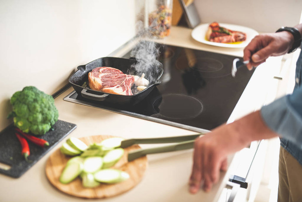 Piece of meat with steam frying on stovetop while man holding fork - Foto, Imagen
