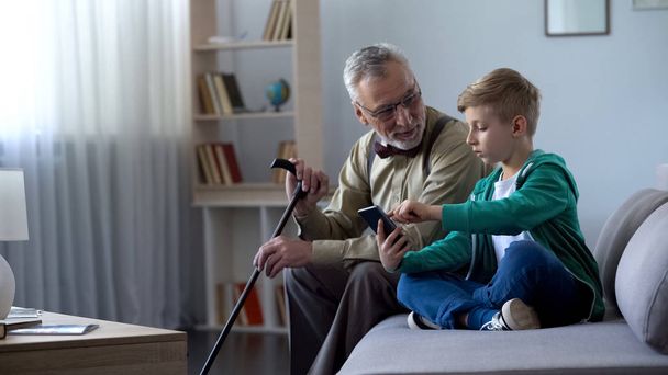 Boy explaining to old man how to use cell phone, simple technologies for old man - Foto, imagen