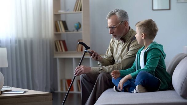 Anciano sosteniendo el teléfono celular, chico ayudándole a familiarizarse con las nuevas tecnologías
 - Foto, Imagen