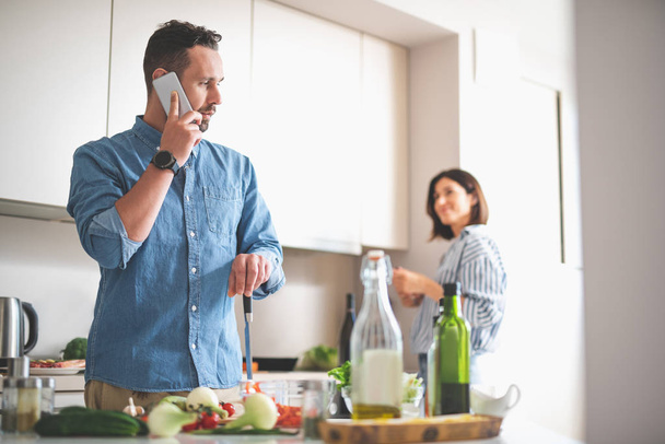 Handsome bearded gentleman talking on cellphone in kitchen - Photo, Image
