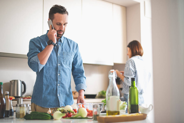 Serious bearded man talking on cellphone in kitchen - Foto, Bild
