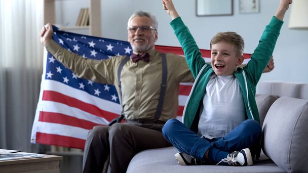 Boy and grandpa waving American flag, watching sport game at home, happy for win - Фото, зображення