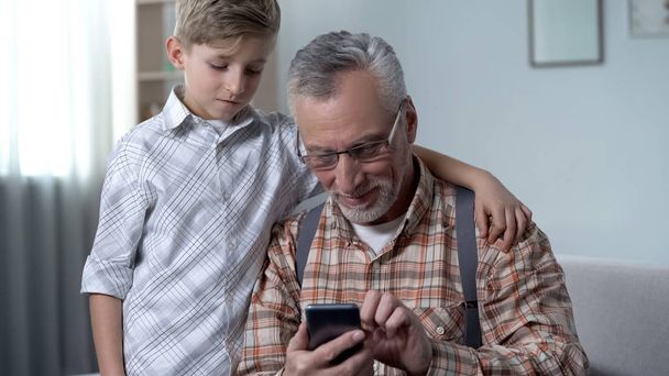 Boy helping grandfather to better understand smartphone, digital generation gap - 写真・画像