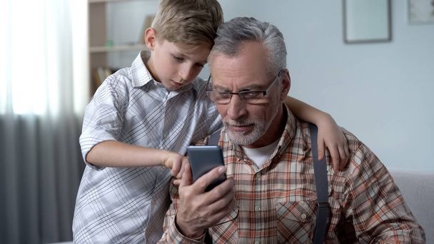 Grandson explaining grandpa how to use smartphone, easy application for elderly - Foto, Imagen
