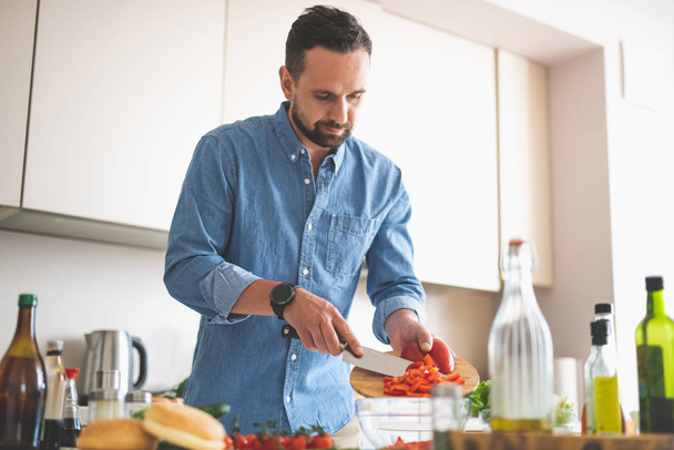Handsome bearded man putting sliced red pepper to bowl - Photo, Image