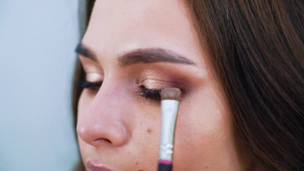 Closeup female hands applying eyeshadows on cute young womans eyelids using special brush - Video