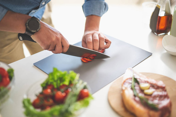 Hombre rebanando chile rojo con cuchillo en tabla de cortar
 - Foto, Imagen