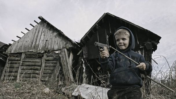 homeless caucasian boy playing with gun in abandoned village - Zdjęcie, obraz