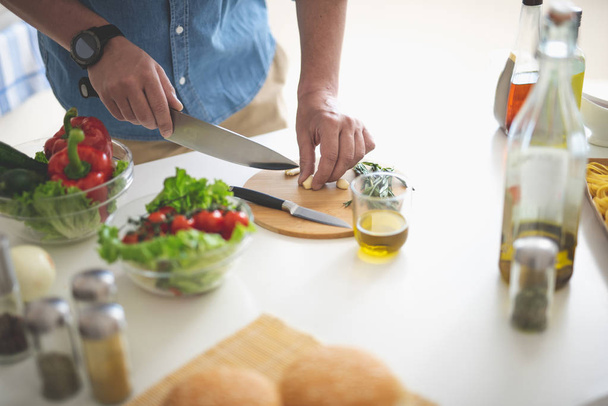 Man chopping garlic with knife on cutting board - Foto, afbeelding