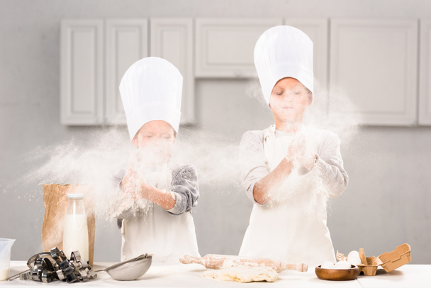 foco seletivo de irmão e irmã em chapéus chef se divertindo com farinha na cozinha
  - Foto, Imagem