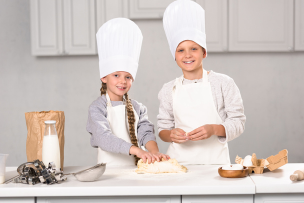 cheerful brother and sister preparing dough for cookies at table in kitchen - Foto, Imagem