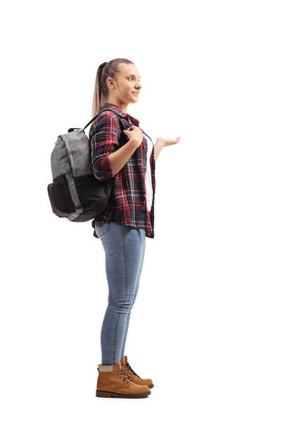 Full length profile shot of a teenage female student standing and gesturing with her hand isolated on white background - Zdjęcie, obraz