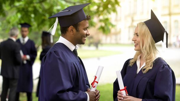 Couple of graduate students with diplomas talking and smiling to each other - Foto, Imagen