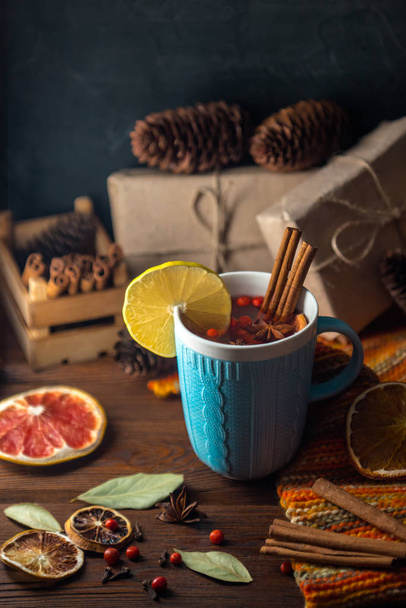 Cosy still life with mulled wine, cinnamon, anise, lemon and dried citrus. Christmas and New Year food and drink composition. Mulled cider in blue ceramic glass, knitted warm textile and given boxes.  - Foto, Imagem