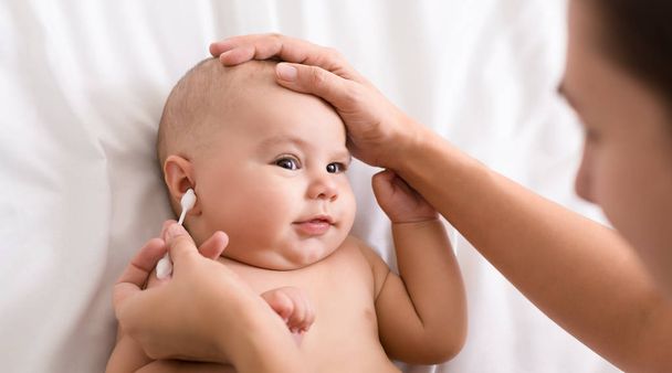 Madre limpiadora de manos oreja de bebé con hisopo de algodón
 - Foto, Imagen