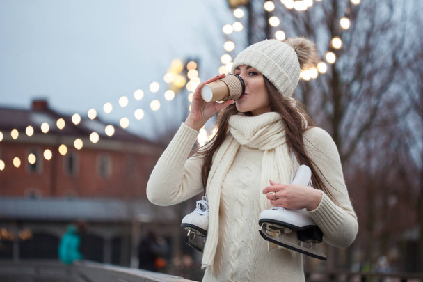 Happy young woman in knitted sweater and hat is going skating and drinks coffee - Foto, imagen