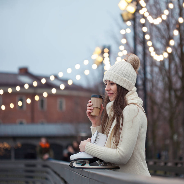 Happy young woman in knitted sweater and hat is going skating and drinks coffee - Foto, imagen