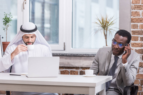 Empresário afro-americano falando em smarthphone perto do parceiro árabe
  - Foto, Imagem
