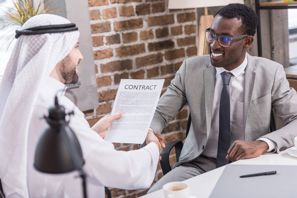 Arabian businessman holding contract and shaking hands with african american partner - Photo, Image