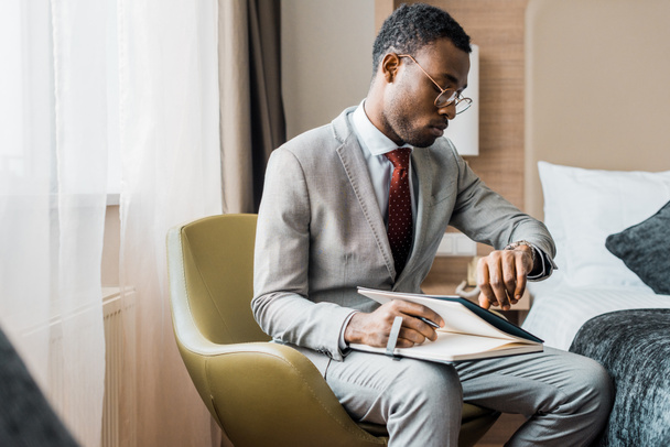 empresário afro-americano em desgaste formal com diário olhando para relógio de pulso
 - Foto, Imagem