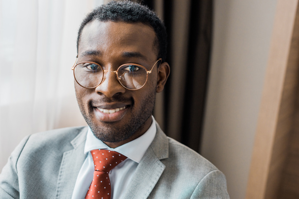 handsome smiling african american businessman in eyeglasses and gray jacket - Valokuva, kuva