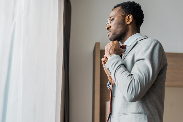 боковой вид африканского бизнесмена, поправляющего красный галстук и смотрящего в окно
 - Фото, изображение