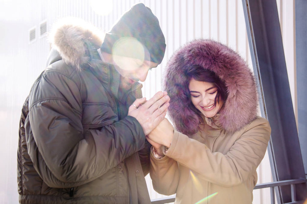 Couple in a winter clothes laugh and enjoy communication. The guy warms girl frozen hands. - Photo, Image