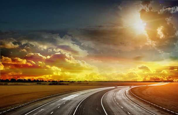   Estrada de asfalto passando por um campo de trigo e alfafa. O pôr-do-sol no horizonte. Natureza antes de uma tempestade. Imagem muito brilhante
 - Foto, Imagem