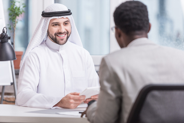 Αραβική επιχειρηματίας χαμογελώντας και κρατώντας ψηφιακή δισκίο στο γραφείο  - Φωτογραφία, εικόνα