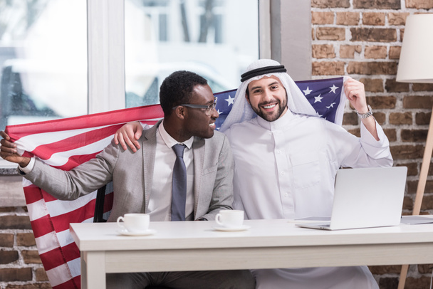 Πολυπολιτισμική επιχειρηματίες κρατώντας αμερικανική σημαία στο σύγχρονο γραφείο  - Φωτογραφία, εικόνα