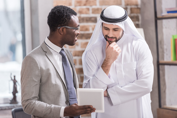 Африканский американский бизнесмен держит цифровой планшет и смотрит на арабского партнера
  - Фото, изображение