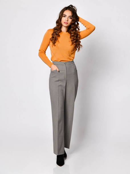 Young beautiful brunette woman posing in new casual orange blouse sweater and grey pants - Fotó, kép