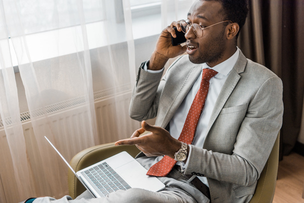 επιτυχημένος επιχειρηματίας αφρικανική αμερικανική μιλώντας στο smartphone και δείχνοντας σε φορητό υπολογιστή  - Φωτογραφία, εικόνα