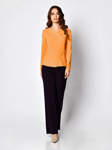 Young beautiful brunette woman posing in new casual yellow orange blouse sweater and black pants - Photo, Image