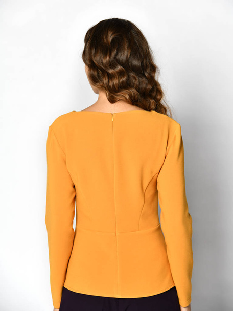 Young beautiful brunette woman posing in new casual yellow orange blouse sweater backside rear view - Zdjęcie, obraz