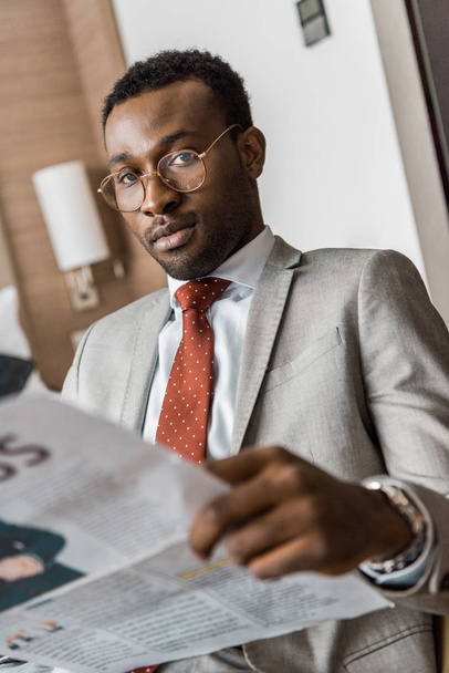 african american businessman in suit holding newspaper and looking at camera - Fotó, kép