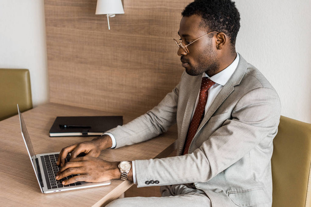 concentrated african american businessman typing on laptop in hotel room - Photo, Image