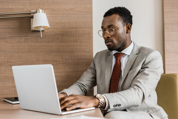 επικεντρώθηκε Αφρικανικός Αμερικανός επιχειρηματίας πληκτρολογώντας σε φορητό υπολογιστή στο δωμάτιο του ξενοδοχείου - Φωτογραφία, εικόνα