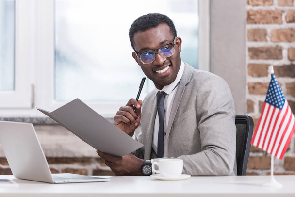 Африканский американский бизнесмен держит папку и ручку в офисе
  - Фото, изображение
