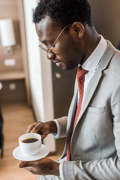 african american businessman looking at cup of coffee in hotel room - Fotó, kép