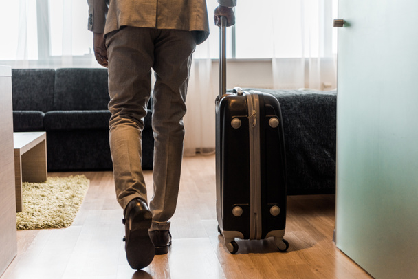 cropped view of businessman in suit with baggage coming into hotel room - Zdjęcie, obraz