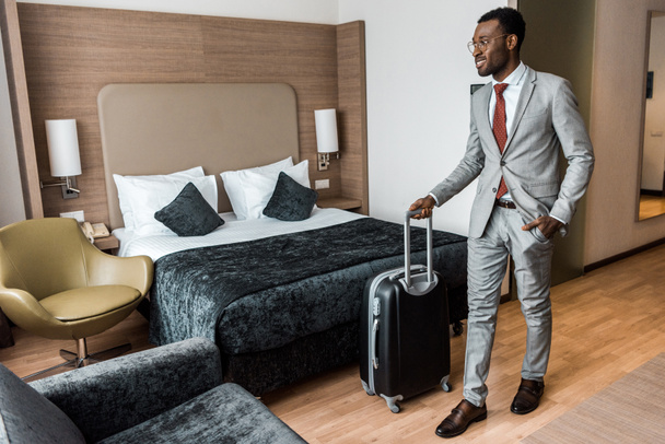 homme d'affaires afro-américain souriant avec sac de voyage dans la chambre d'hôtel
 - Photo, image