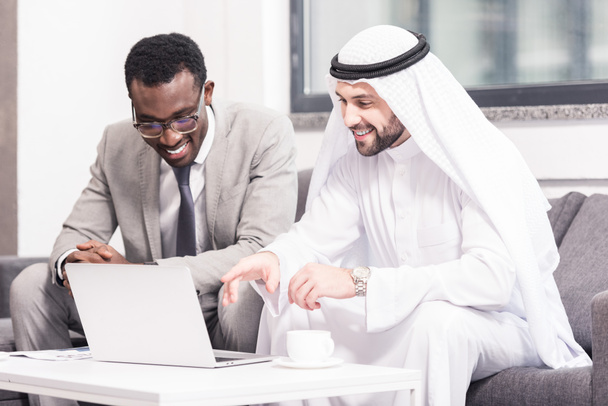 Hombre de negocios árabe mirando portátil con socio afroamericano en la oficina
  - Foto, imagen