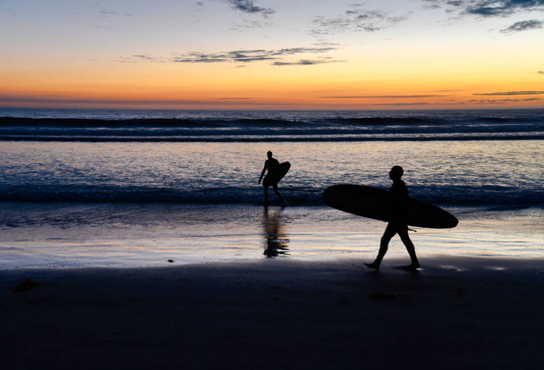Deux silhouettes de surfeurs portant des planches de surf au coucher du soleil
 - Photo, image
