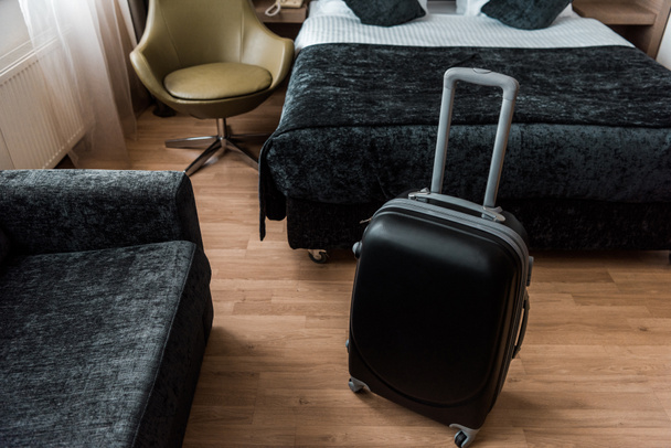 schwarzer Reisekoffer im Hotelzimmer mit Bett und Sessel - Foto, Bild