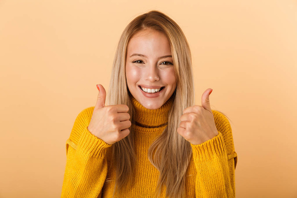 Portrait of a lovely young woman dressed in sweater standing isolated over yellow background, giving thumbs up - Fotoğraf, Görsel