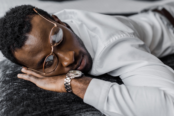 african american man in eyeglasses lying on bed - 写真・画像