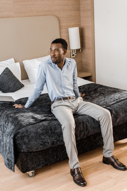 beau jeune homme afro-américain assis sur le lit dans la chambre d'hôtel
 - Photo, image